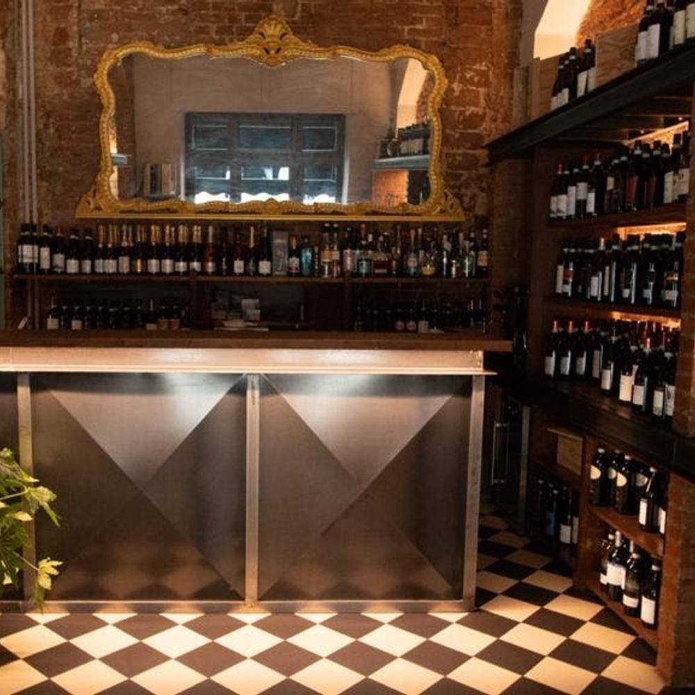 Il bar con lo specchio dalla cornice dorata, le bottiglie di vino sugli scaffali e il pavimento a scacchi