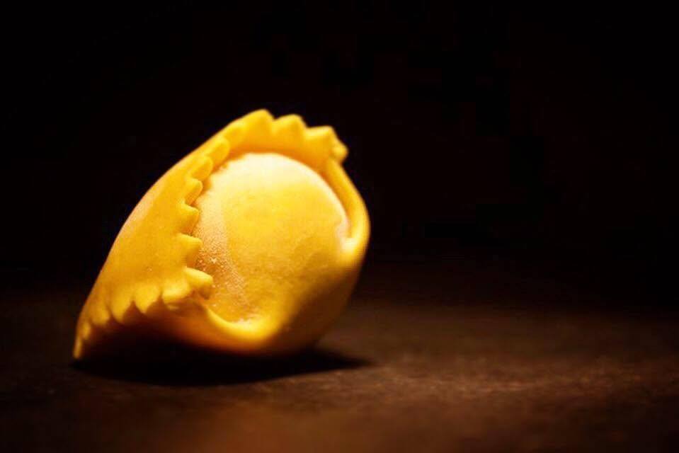 Un plin fatto a mano, pasta gialla pizzicata, su fondo scuro