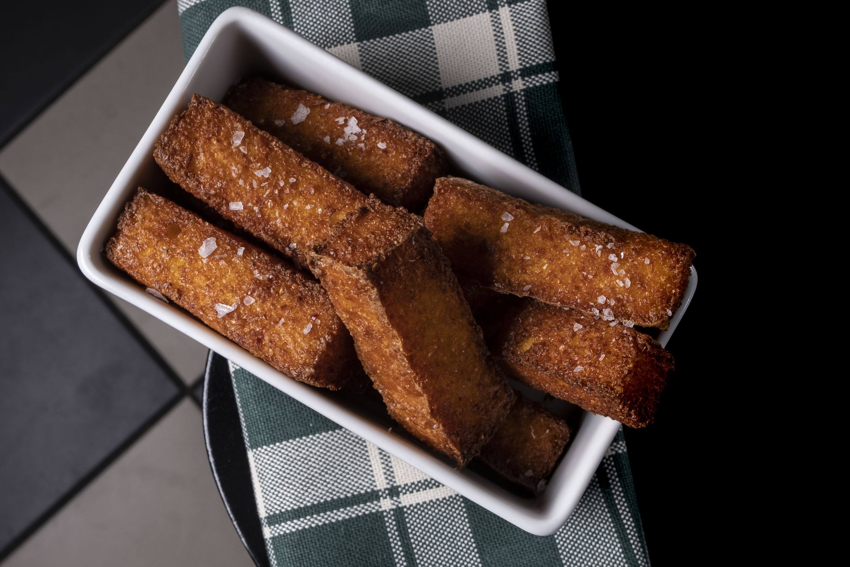 Bastoncini di polenta fritta con sale grosso in una vaschetta bianca su un canovaccio verde