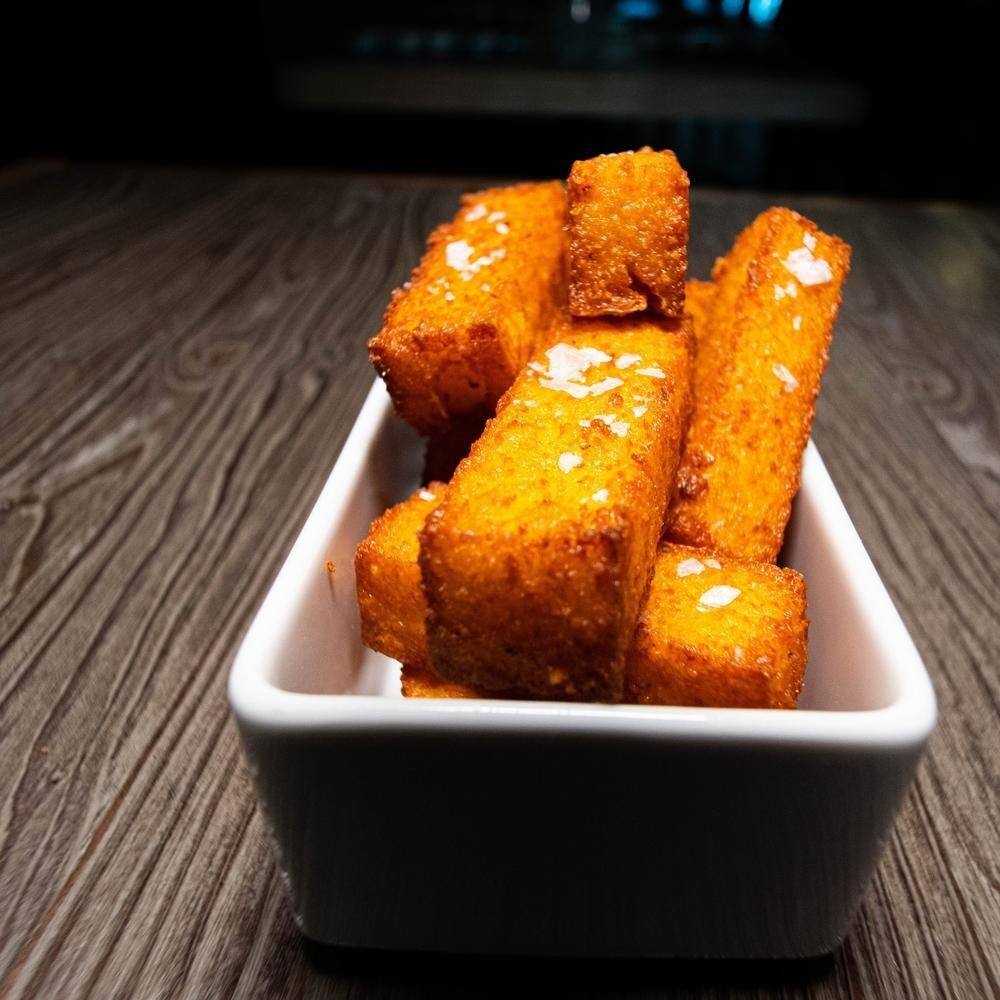 Polenta fritta dorata in una vaschetta bianca su un tavolo di legno