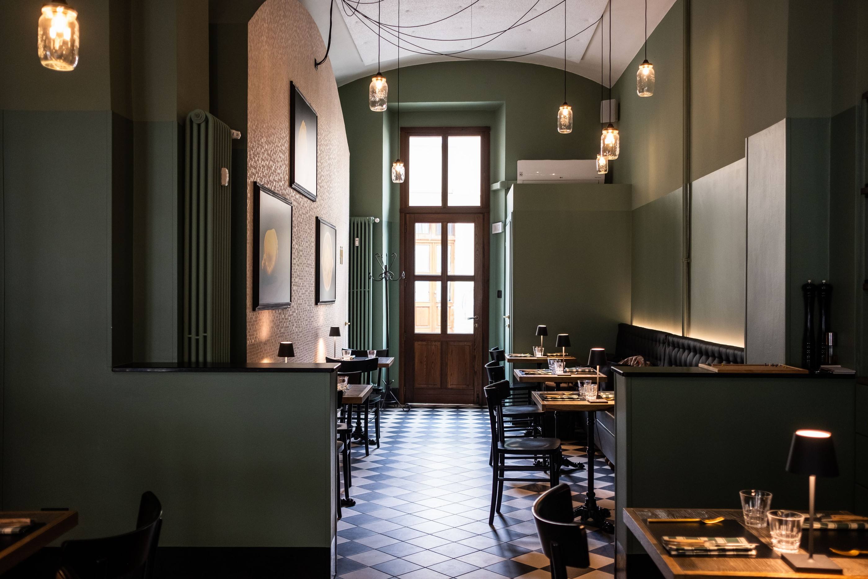 La sala di Madama Piola: pareti verde salvia, pavimento a scacchi bianchi e neri, lampade a sospensione e tavoli apparecchiati